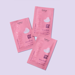 Trzy różowe opakowania "Kimoco Lift-Up Skin Melting Eye Lift Patches" ułożone obok siebie w różnych kątach, na jasnofioletowym tle.