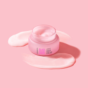 Zdjęcie na różowym tle: po środku otwarty słoiczek "Kimoco Glass Skin Luminous Aqua Cream" z kremem na wierzchu, z lewej i z prawej rozsmarowane pasma tego samego kremu.