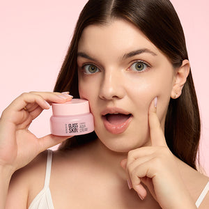 Zdjęcie na jasnoróżowym tle: z lewej kobieta trzymająca różowy słoiczek "Kimoco Glass Skin Luminous Aqua Cream" przy policzku, z prawej jej dłoń dotykająca drugiego policzka, twarz ze zdziwionym wyrazem i uchylonymi ustami.
