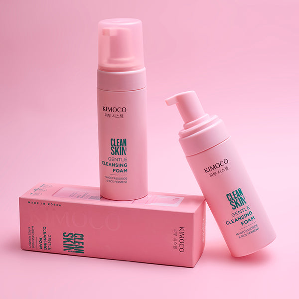 Dwie różowe butelki z pompką kosmetyku Kimoco Clean Skin Gentle Cleansing Foam stojące na różowym pudełku, na różowym tle.
