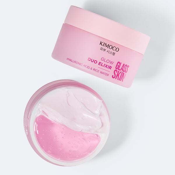 Zdjęcie na jasnoszarym tle: u góry przekrzywiona pokrywka słoiczka "Kimoco Glass Skin Glow Duo Elixir", u dołu otwarty słoiczek widziany z góry z dwoma masami — białym kremem i różowym żelem.
