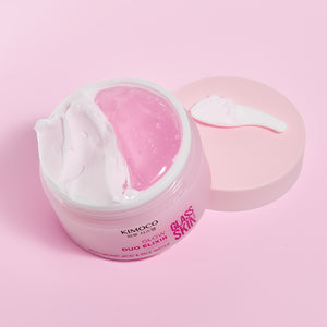 Zdjęcie na różowym tle: z lewej otwarty słoiczek "Kimoco Glass Skin Glow Duo Elixir" z widocznym białym kremem i różowym żelem, z prawej odłożona pokrywka z odrobiną kremu na wierzchu.