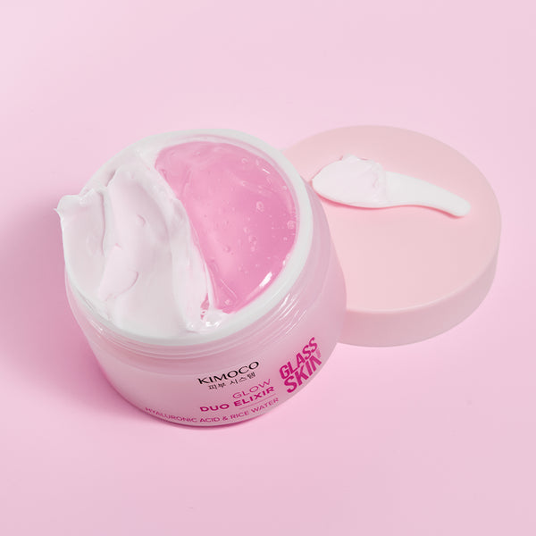 Zdjęcie na różowym tle: z lewej otwarty słoiczek "Kimoco Glass Skin Glow Duo Elixir" z widocznym białym kremem i różowym żelem, z prawej odłożona pokrywka z odrobiną kremu na wierzchu.