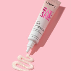 Zdjęcie na różowym tle: u góry ułożona ukośnie tuba "Kimoco Glass Skin Bright Eyes Illuminator", u dołu wyciśnięty z niej rozświetlający produkt w kształcie faliście ułożonej linii z widocznym brokatem.