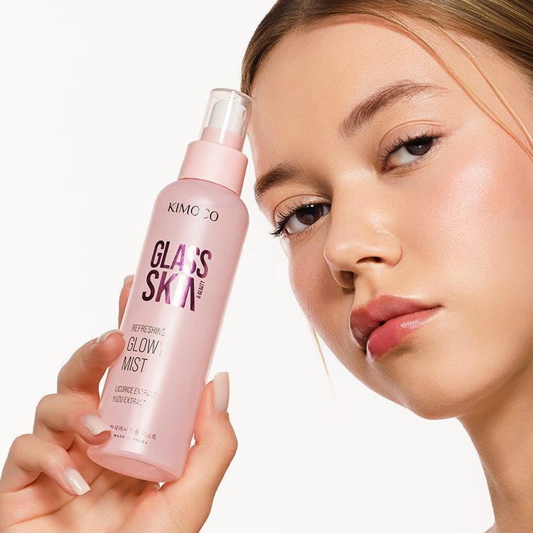 Różowa butelka z rozpylaczem kosmetyku Kimoco Glass Skin Refreshing Glowy Mist z ekstraktem lukrecji i yuzu, ozdobiona białymi kropkami, na jasnoszarym tle