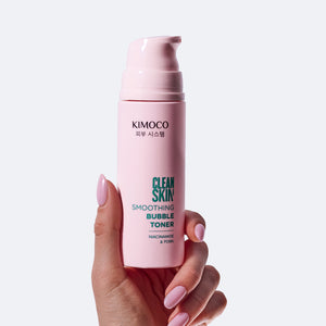 Po środku dłoń trzymająca różową butelkę kosmetyku Kimoco Clean Skin Smoothing Bubble Toner, na białym tle