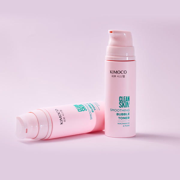 Zdjęcie na jasnoróżowym tle: z prawej stojąca różowa butelka "Kimoco Clean Skin Smoothing Bubble Toner" z dozownikiem, z lewej taka sama butelka leżąca na boku.