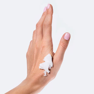 Po środku dłoń z różowym manicure, na której znajduje się biały balsam, na białym tle.