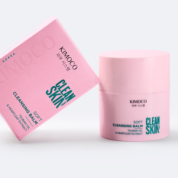 Po środku różowe pudełko oparte o różowy słoiczek kosmetyku Clean Skin Soft Cleansing Balm, na szarym tle.