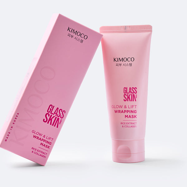 Różowe pudełko oparte o różową tubę kosmetyku Glass Skin Glow & Lift Wrapping Mask, na szarym tle.