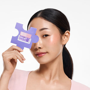 Twarz kobiety z fioletowym elementem w kształcie puzzla zasłaniającym jedno oko, na którym widnieje zdjęcie słoiczka Kimoco Lift-Up Skin, na białym tle